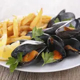 Moules frites sur une assiette blanche avec des quartiers de citron et du persil. Un plat classique, quel vin avec moules frites ?