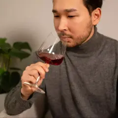 Un homme déguste un verre de vin rouge, réfléchissant à ce que contient le vin. Une plante verte est visible en arrière-plan.