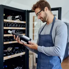Un homme examine une bouteille de vin devant une cave à vin électrique, illustrant comment ranger une cave à vin électrique.
