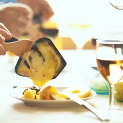Raclette fondue dégoulinant sur des pommes de terre, un verre de vin blanc de Pouilly-Fumé à côté.