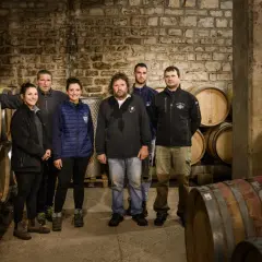 L'équipe du domaine Ramonet pose fièrement dans la cave, entourée de fûts de chêne prêts à accueillir le vin.