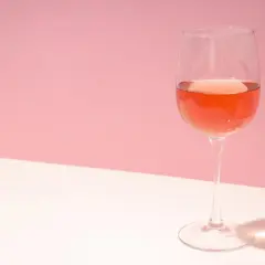 Un verre de vin rosé, dont la couleur suggère qu'il est fait avec quel raisin, sur fond rose et blanc.