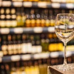 Verre à vin vide sur un comptoir, devant des étagères remplies de bouteilles. Une mise en avant foire aux vins qui invite à la dégustation.