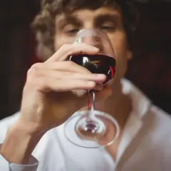 Un homme déguste un verre de vin rouge, réfléchissant aux termes pour qualifier le vin.