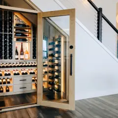Belle cave à vin moderne sous un escalier, avec des étagères en bois et des bouteilles illuminées.
