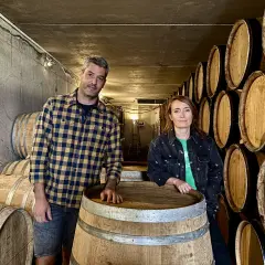Un homme et une femme posent devant des tonneaux dans la cave du domaine Bott.