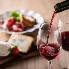 Un verre de vin rouge est servi, accompagné d'un plateau de fromages et de charcuterie. Un apéritif à base de vin parfait pour partager.