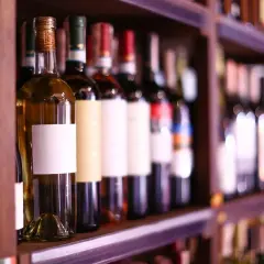Étagères remplies de bouteilles de vin, certaines avec des étiquettes blanches vierges, prêtes à accueillir le meilleur cépage de vin rouge.
