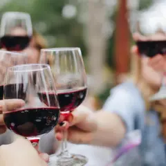 Des mains portent des verres de vin rouge pour un toast. Un moment convivial autour d'un vin doux apéritif.