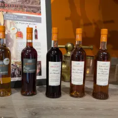 Cinq bouteilles de Pineau des Charentes Drouet, dont le meilleur pineau des Charentes, sur un fond de promotion du domaine.