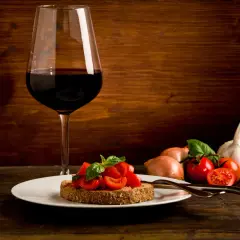 Bruschetta aux tomates fraîches et basilic, accompagnée d'un verre de vin rouge passe partout. Ail et oignons en arrière-plan.