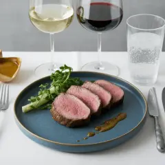 Filet mignon de porc tranché, servi avec une sauce et des verdures, accompagné de vin blanc et rouge.