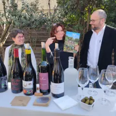 Trois personnes souriantes devant une table garnie de bouteilles de vin, de verres et d'un magazine.