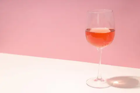 Un verre de vin rosé, dont la couleur suggère qu'il est fait avec quel raisin, sur fond rose et blanc.