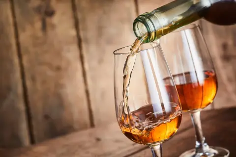 Un verre se remplit d'un vin paillé ambré, un autre verre déjà plein est à côté.