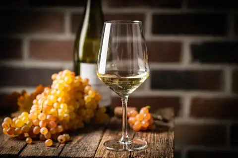 Verre de vin blanc, grappes de raisins dorés et bouteille sur fond de briques. Le chardonnay est-il un vin sec ? La réponse est dans le verre.