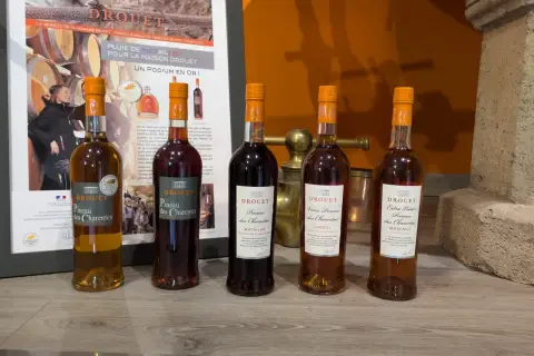 Cinq bouteilles de Pineau des Charentes Drouet, dont le meilleur pineau des Charentes, sur un fond de promotion du domaine.