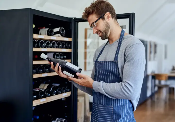Un homme examine une bouteille de vin devant une cave à vin électrique, illustrant comment ranger une cave à vin électrique.