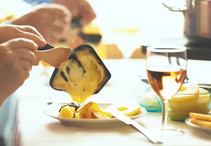 Raclette fondue dégoulinant sur des pommes de terre, un verre de vin blanc de Pouilly-Fumé à côté.
