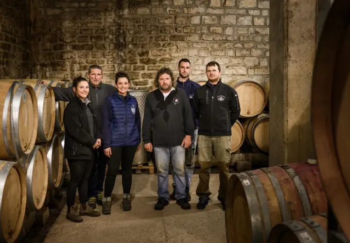 L'équipe du domaine Ramonet pose fièrement dans la cave, entourée de fûts de chêne prêts à accueillir le vin.