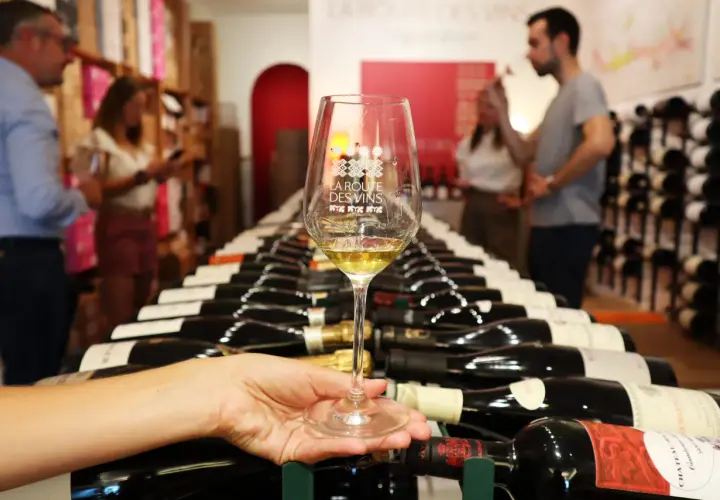 Verre de vin blanc sur fond de bouteilles alignées, évoquant les plaisirs de la route des vins.