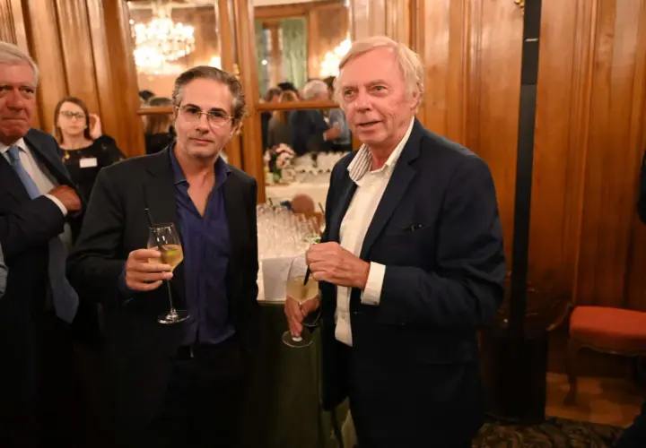 Alain Marty, à droite, avec un verre à la main, discute avec un homme à lunettes.