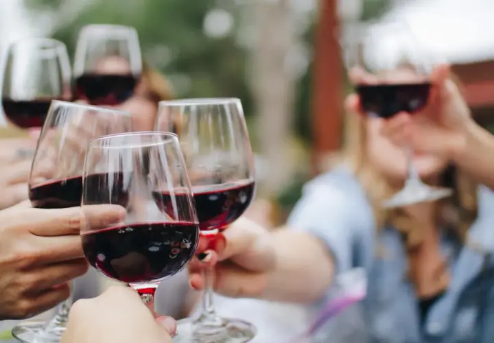 Des mains lèvent des verres de vin rouge pour un apéro convivial.