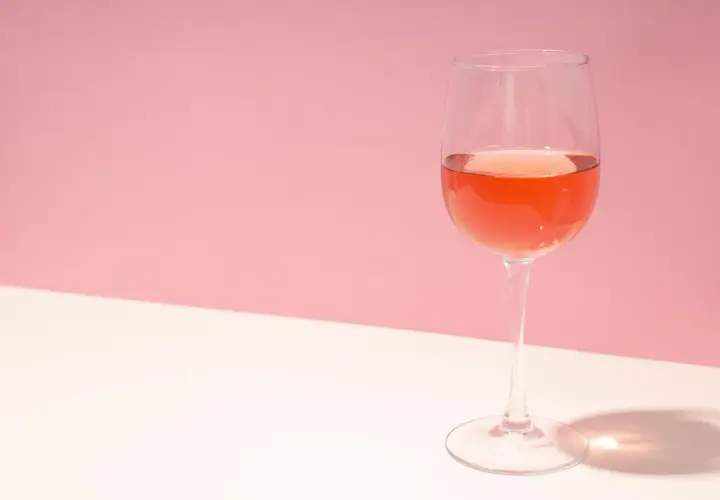 Un verre de vin rosé, dont la couleur suggère qu'il est fait avec quel raisin, sur fond rose et blanc.