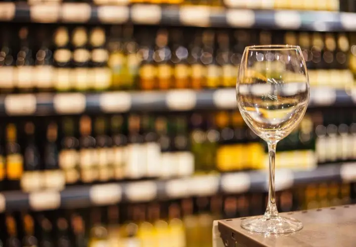 Verre à vin vide sur un comptoir, devant des étagères remplies de bouteilles. Une mise en avant foire aux vins qui invite à la dégustation.