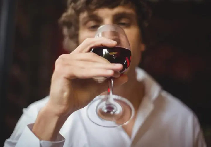 Un homme déguste un verre de vin rouge, réfléchissant aux termes pour qualifier le vin.