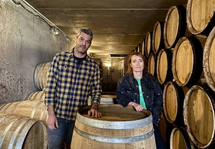 Un homme et une femme posent devant des tonneaux dans la cave du domaine Bott.
