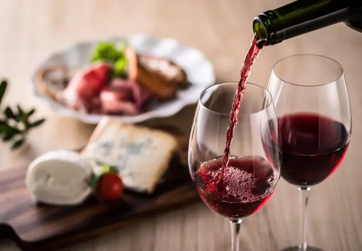 Un verre de vin rouge est servi, accompagné d'un plateau de fromages et de charcuterie. Un apéritif à base de vin parfait pour partager.