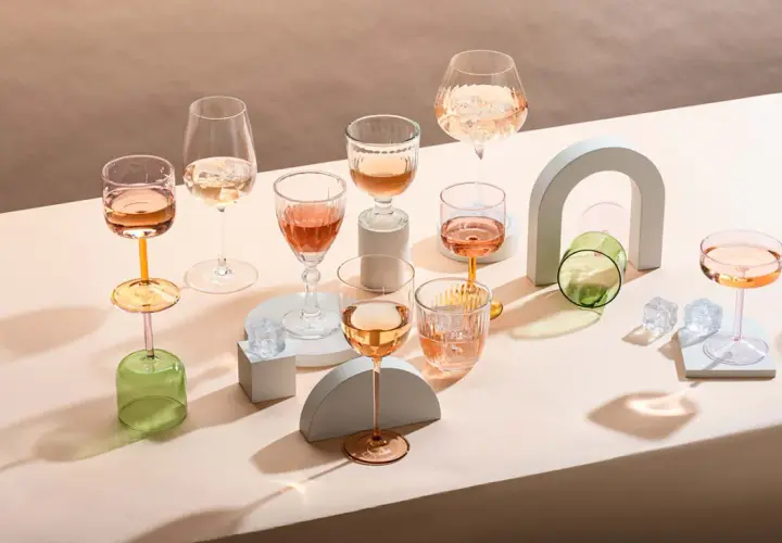 Plusieurs verres de vin blanc ou rosé, certains avec des glaçons, sont disposés sur un fond neutre.