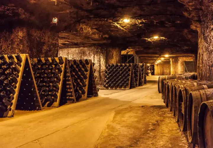 Intérieur d'une cave troglodyte, avec des rangées de bouteilles de vin sur des pupitres et des tonneaux en bois.