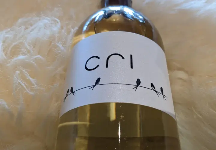 Bouteille de vin blanc "Cri" sur fond doux et texturé. Quatre petits oiseaux stylisés sont perchés sur un fil.