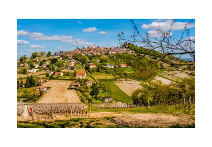 Paysage bucolique de la région de Sancerre, avec un village perché sur une colline, entouré de vignobles et de champs verdoyants sous un ciel bleu.