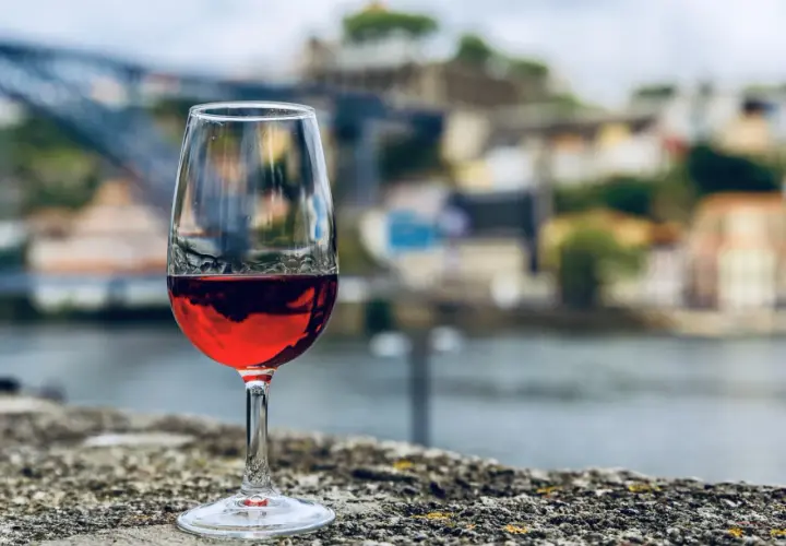 Verre de vin rouge sur un muret, avec la ville de Porto et le fleuve en arrière-plan. Une belle dégustation vin porto.