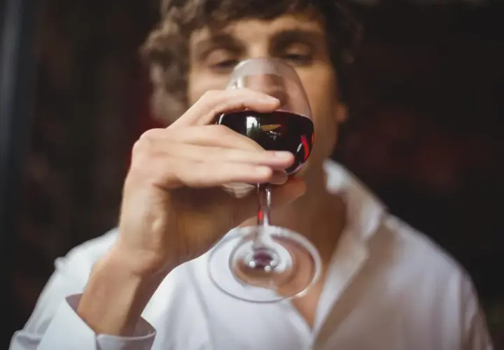 Un homme déguste un verre de vin rouge, savourant le langage du vin.
