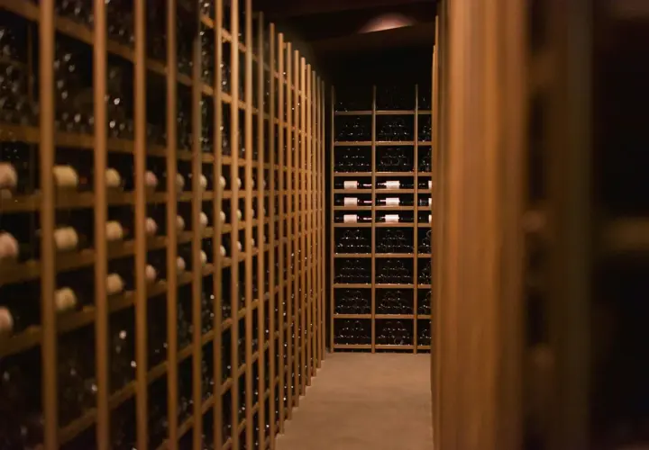 Cave à vin sombre remplie de bouteilles. Des étagères en bois alignent les murs, certaines contenant des bouteilles de vin de garde 20 ans.