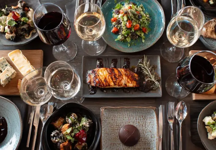 Une table dressée avec des plats variés et des verres de vin rouge et blanc. Une invitation à découvrir la fiche technique accord mets et vins.
