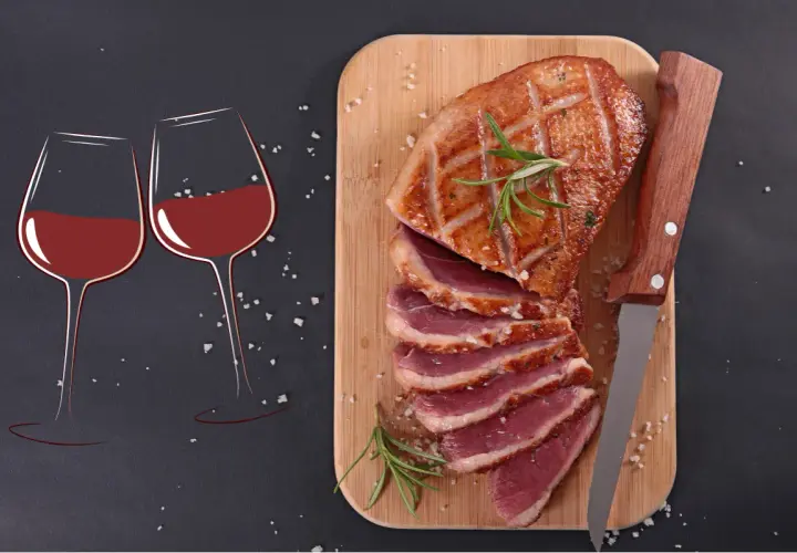 Un plat de magret de canard tranché, garni de romarin, prêt à être dégusté avec deux verres de vin rouge.