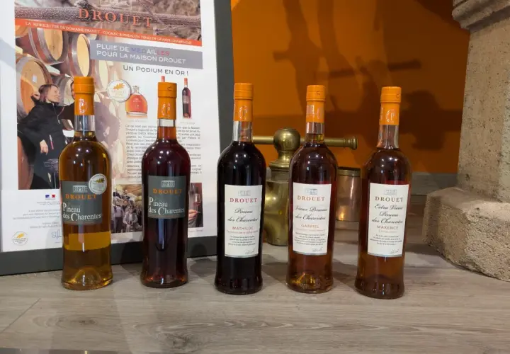 Cinq bouteilles de Pineau des Charentes Drouet, dont le meilleur pineau des Charentes, sur un fond de promotion du domaine.