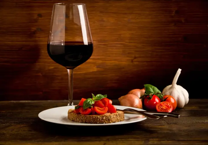 Bruschetta aux tomates fraîches et basilic, accompagnée d'un verre de vin rouge passe partout. Ail et oignons en arrière-plan.