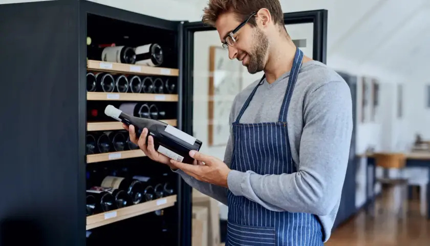 Un homme examine une bouteille de vin devant une cave à vin électrique, illustrant comment ranger une cave à vin électrique.