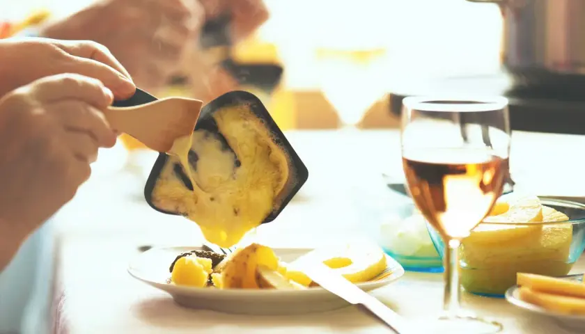 Raclette fondue dégoulinant sur des pommes de terre, un verre de vin blanc de Pouilly-Fumé à côté.