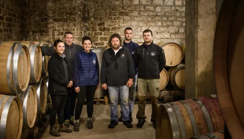 L'équipe du domaine Ramonet pose fièrement dans la cave, entourée de fûts de chêne prêts à accueillir le vin.