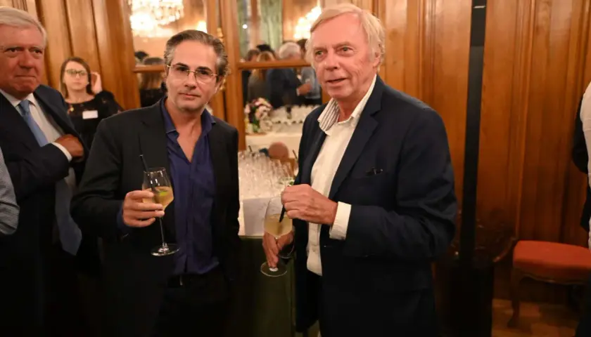 Alain Marty, à droite, avec un verre à la main, discute avec un homme à lunettes.