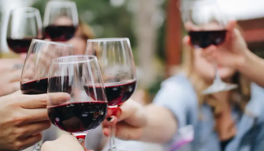 Des mains lèvent des verres de vin rouge pour un apéro convivial.