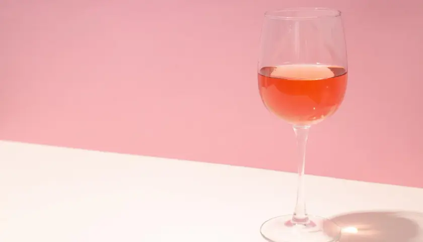 Un verre de vin rosé, dont la couleur suggère qu'il est fait avec quel raisin, sur fond rose et blanc.