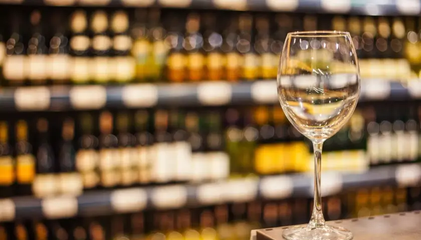 Verre à vin vide sur un comptoir, devant des étagères remplies de bouteilles. Une mise en avant foire aux vins qui invite à la dégustation.